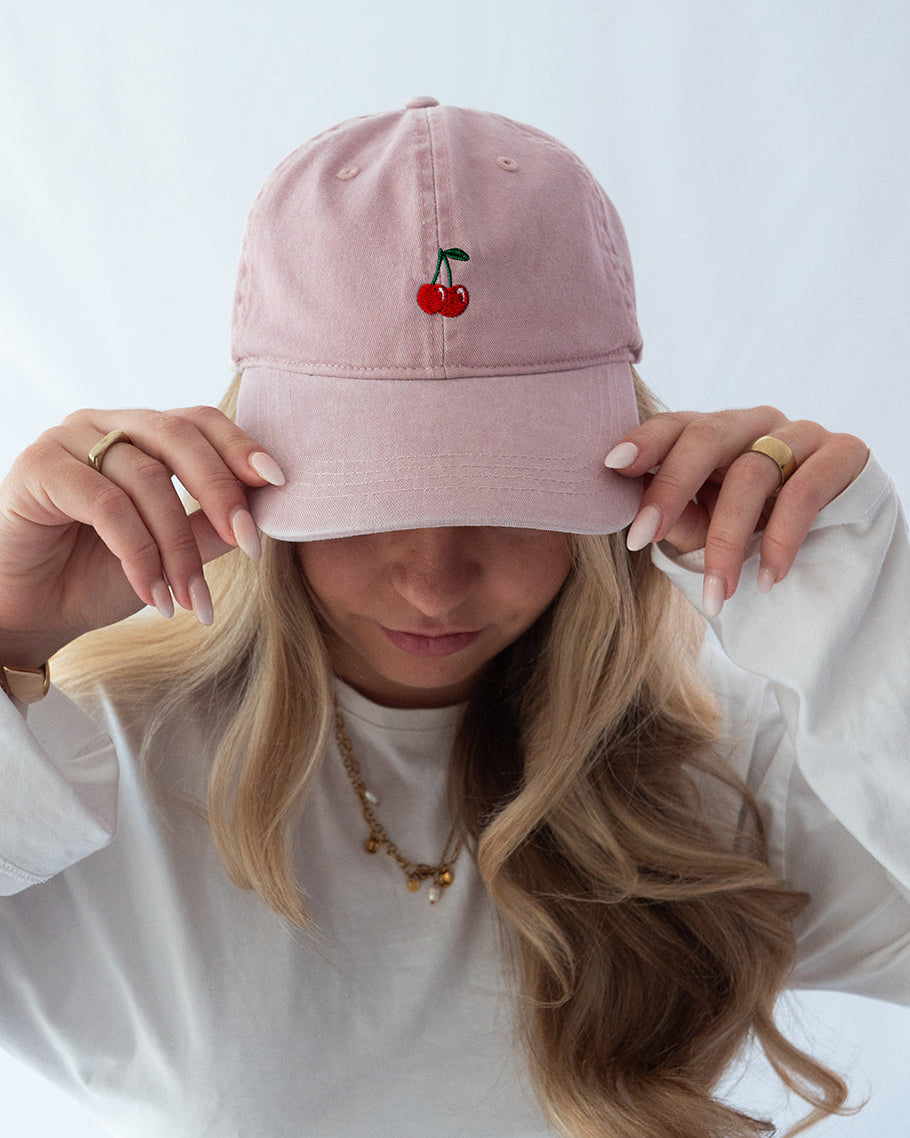 Das Model trägt eine rosa Vintage Cap mit dezent gesticktem Kirschen Motiv