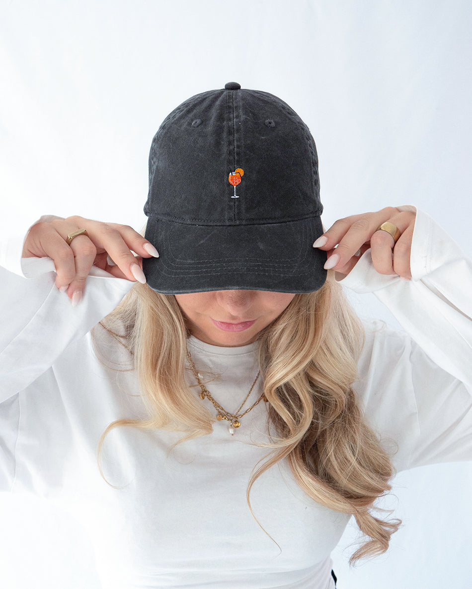 Das Model trägt eine schwarze Vintage Cap mit dezent gesticktem Aperol Spritz Motiv