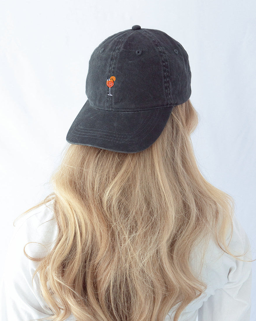 Das Model trägt eine schwarze Vintage Cap mit dezent gesticktem Aperol Spritz Motiv rückwärts