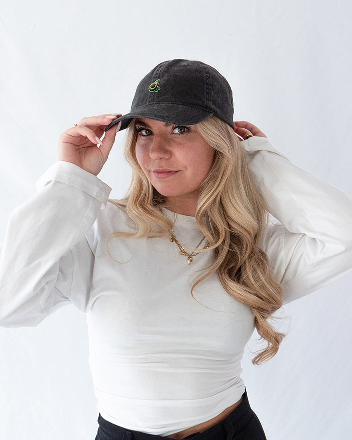 Das Model trägt eine schwarze Vintage Cap mit gesticktem Avocado Motiv in Profil Ansicht