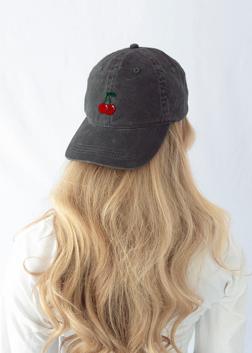 Das Model trägt eine schwarze Vintage Cap mit dezent gesticktem Kirschen Motiv rückwärts