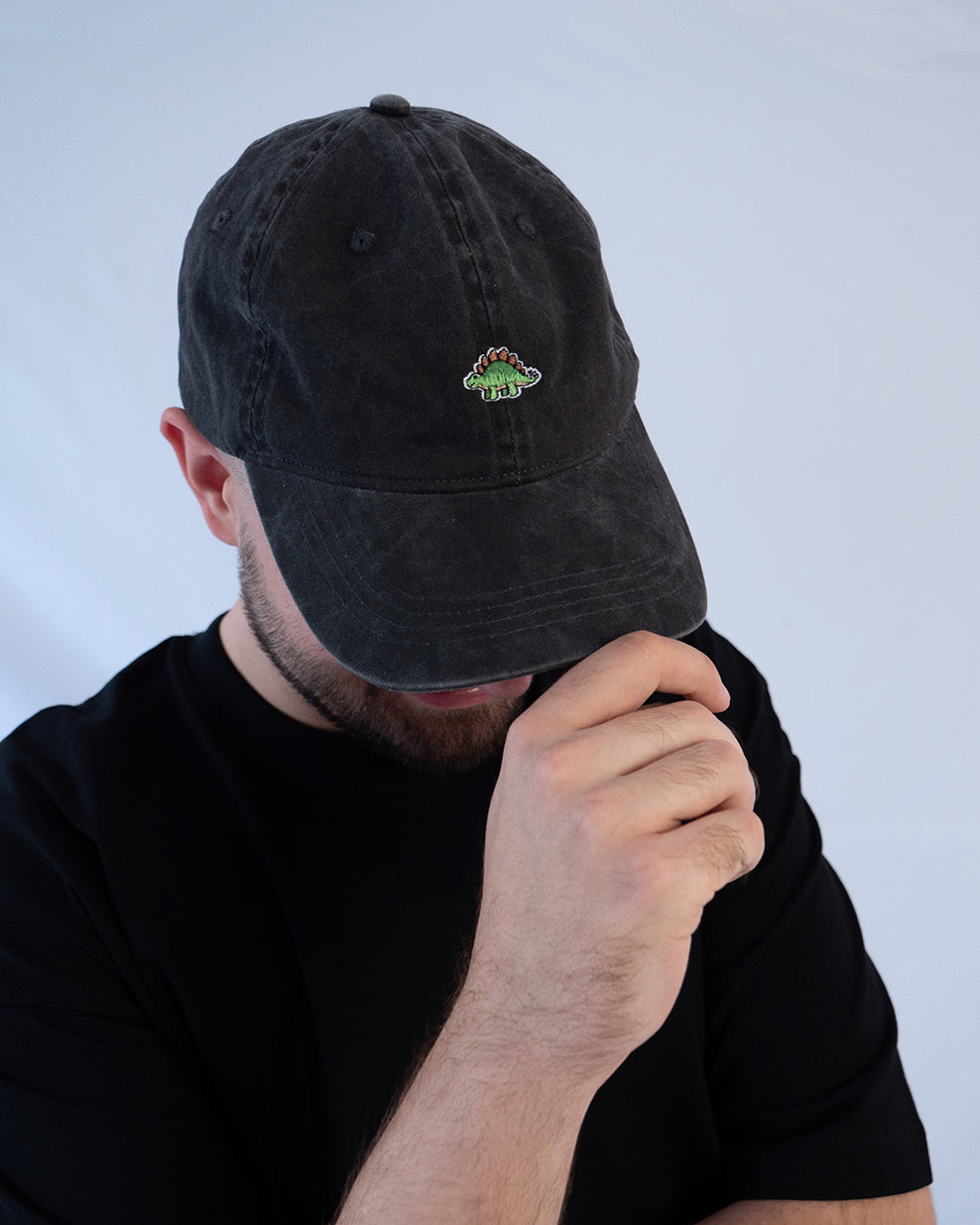 Das Model trägt eine schwarze Vintage Cap mit besticktem Stegosaurus Motiv