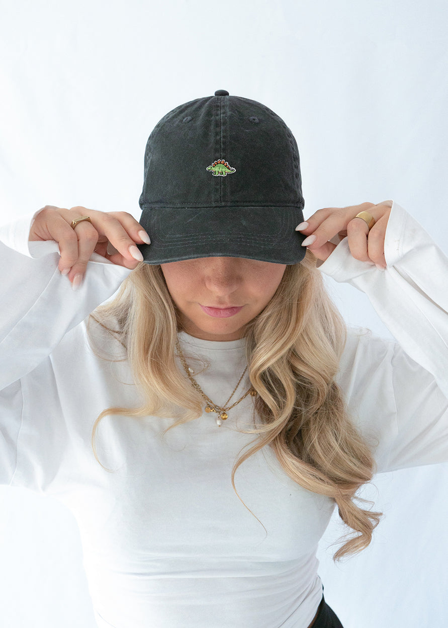 Das Model trägt eine schwarze vintage Cap mit dezent gesticktem Stegosaurus Motiv
