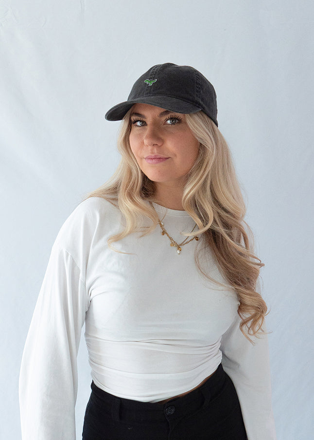 Das Model trägt eine schwarze Vintage Cap mit dezent gesticktem T-Rex Motiv aus einer leichten Profilansicht