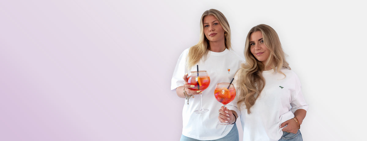Die Model tragen weiße oversize Baumwoll Shirts mit den gestickten Aperol Spritz und T-Rex Motiven auf der Brust