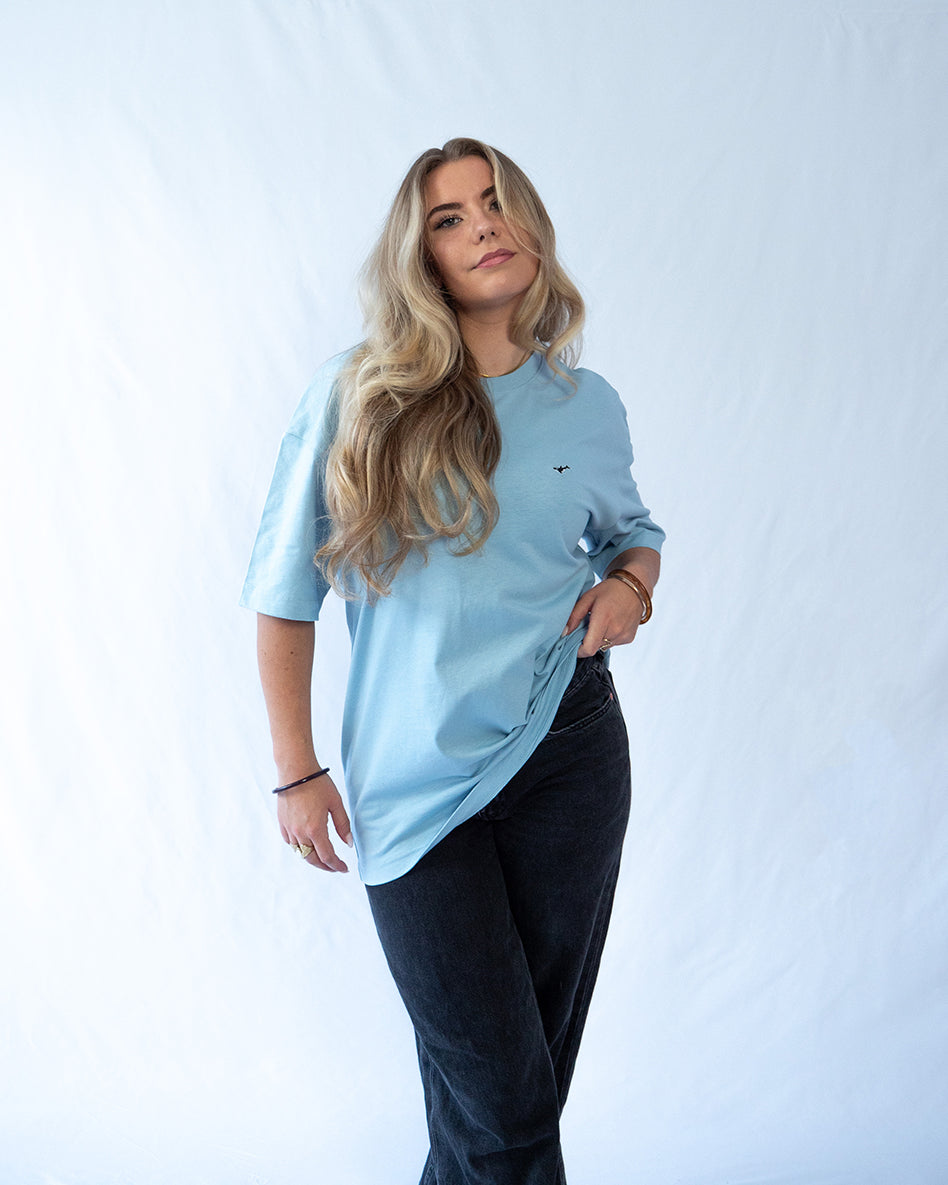 Das Model trägt ein hellblaues oversize Bio-Baumwoll T-Shirt mit gesticktem Orca Motiv auf der Brust