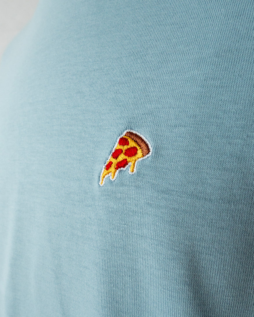 Nahaufnahme des gestickten Pizza Stück Motivs auf blauem T-Shirt