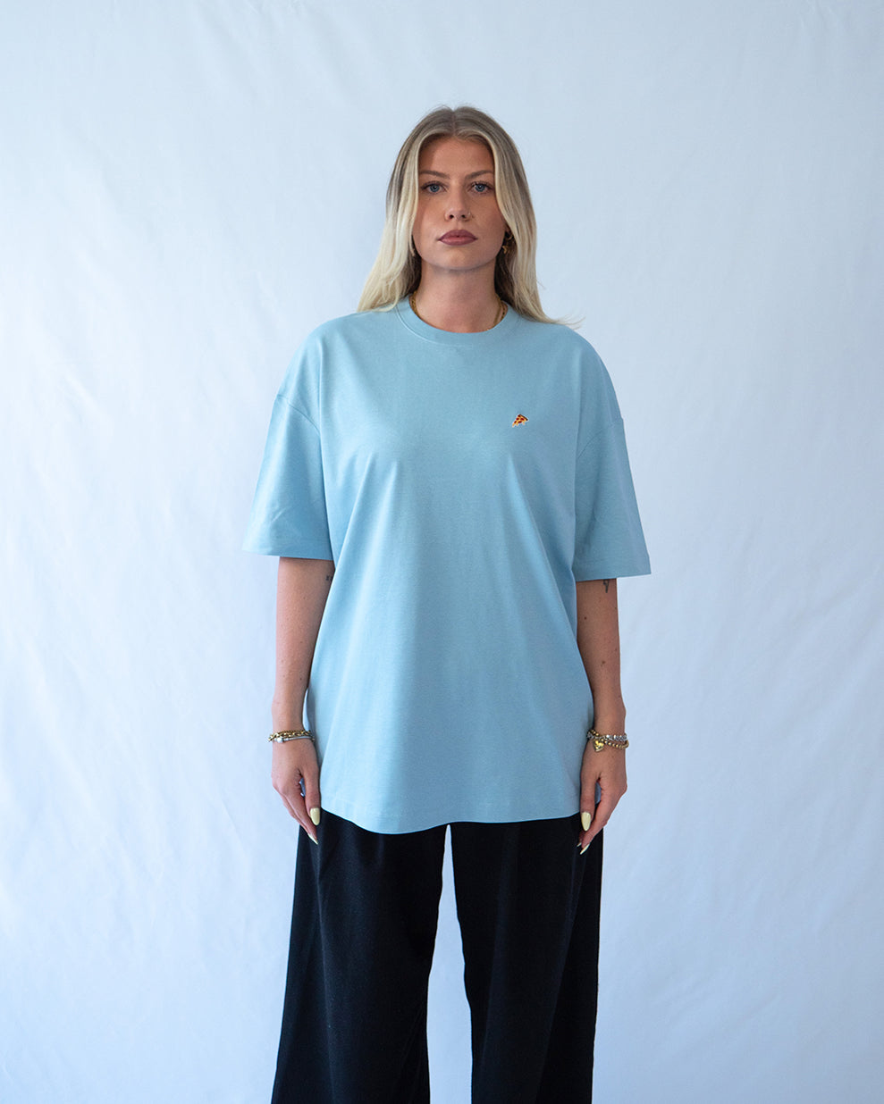 Das Model trägt ein blaues Bio-Baumwoll T-Shirt mit gesticktem Pizza Slice Motiv auf der Brust