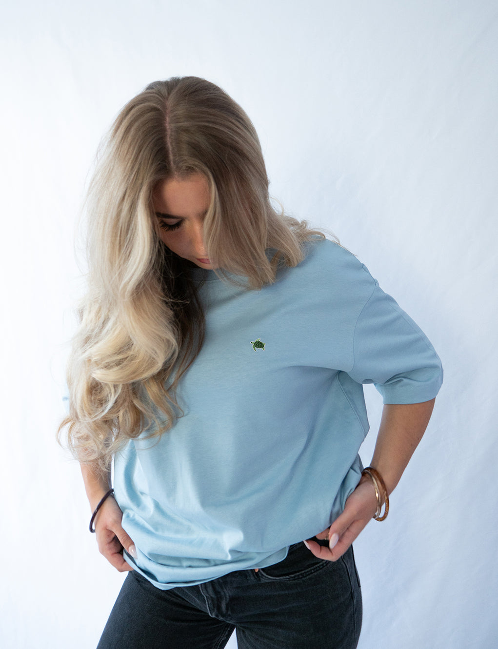 Das Model trägt ein hellblaues oversize Bio-Baumwoll T-Shirt mit dem gestickten Schildkröten Motiv auf der Brust