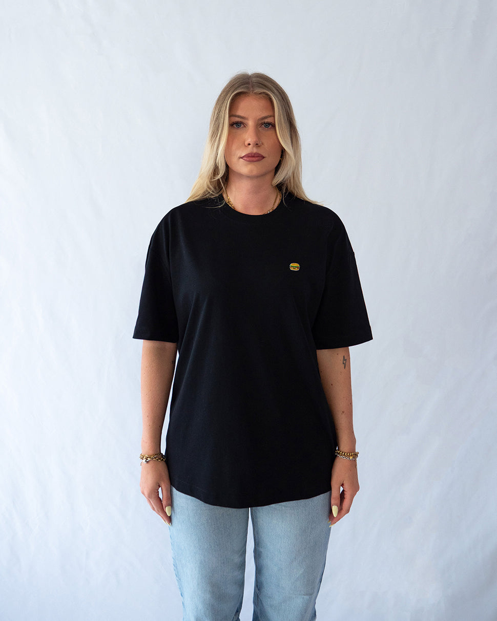 Das Model trägt ein schwarzes Bio-Baumwoll T-Shirt mit gesticktem Burger Motiv auf der Brust