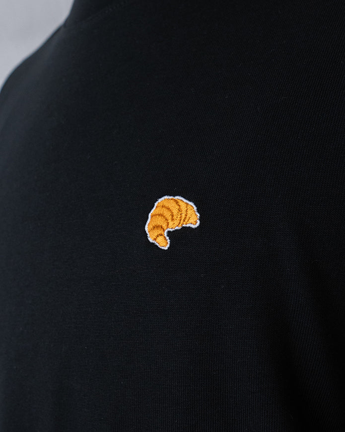 Nahaufnahme des gestickten Croissant Motivs auf schwarzem T-Shirt