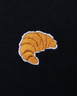 Nahaufnahme des gestickten Croissant Motivs auf schwarzem T-Shirt