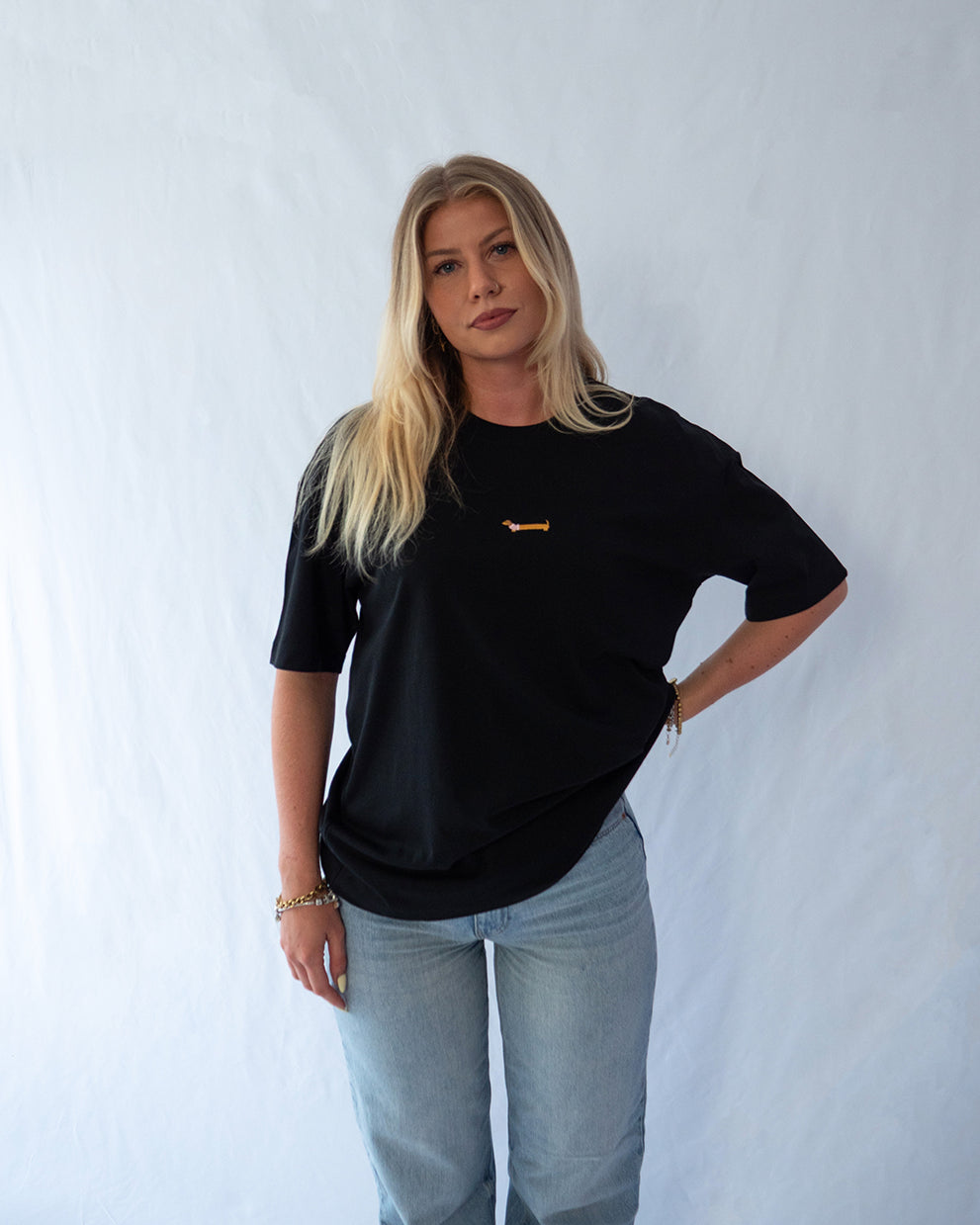 Das Model trägt ein schwarzes oversize Bio-Baumwoll T-Shirt mit gesticktem Dackel Motiv zentriert auf der Brust