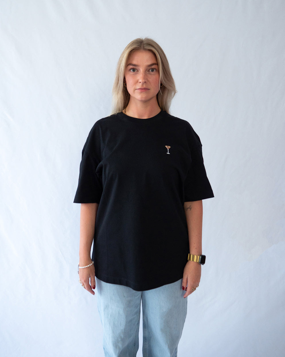 Das Model trägt ein schwarzes Bio-Baumwoll T-Shirt mit gesticktem Espresso Martini Cocktail Motiv auf der Brust