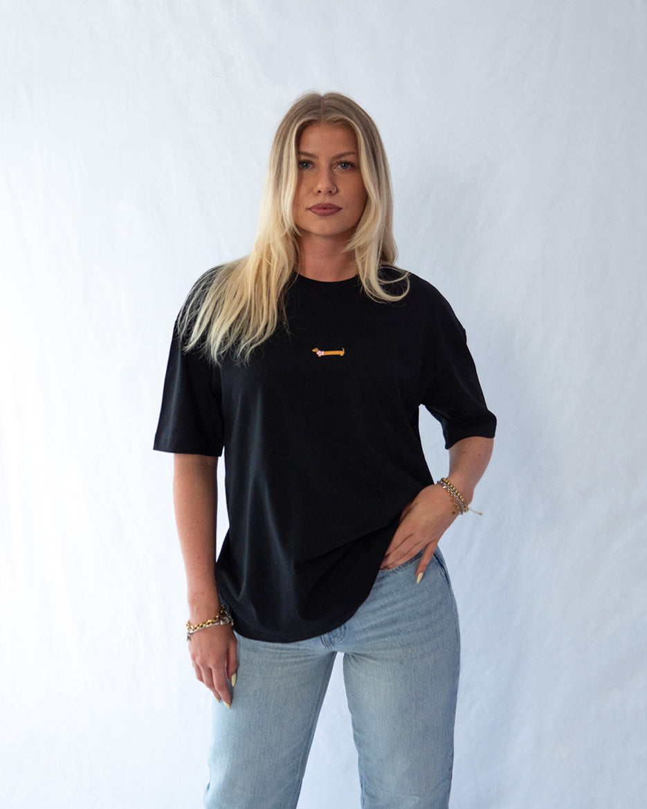 Das Model trägt ein schwarzes oversize Bio-Baumwoll T-Shirt mit gesticktem Dackel Motiv zentriert auf der Brust