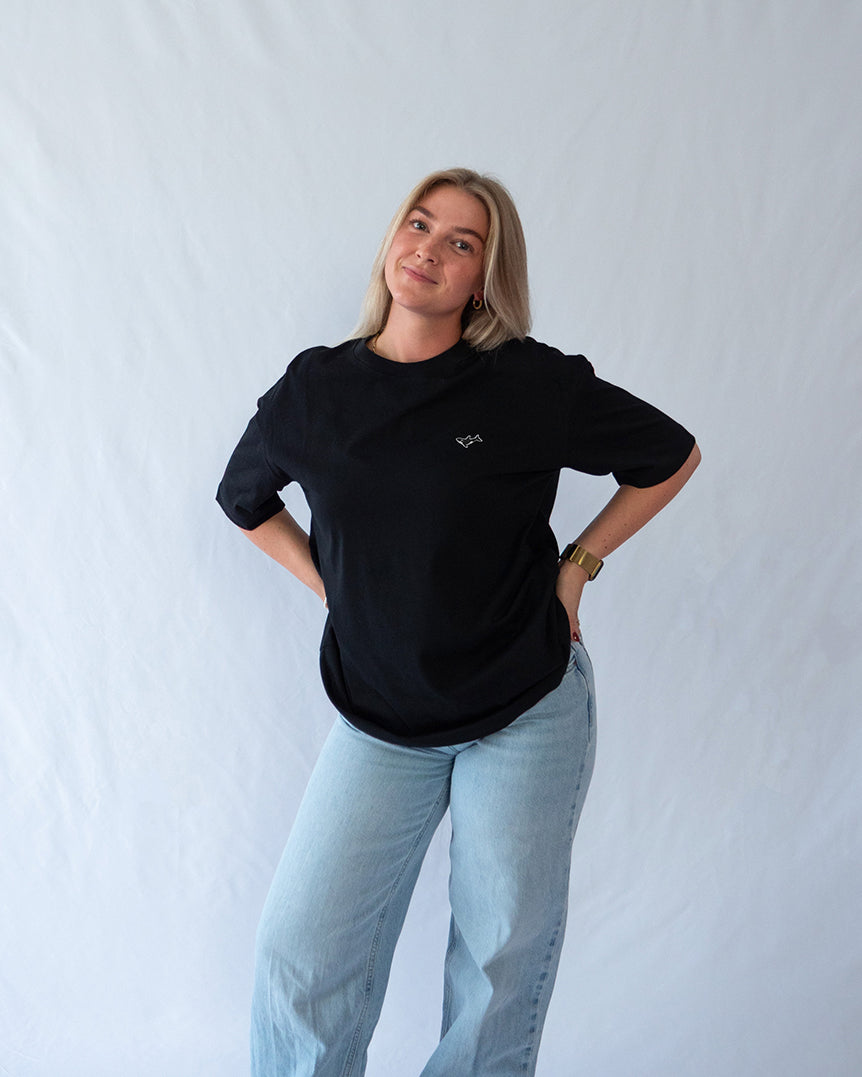 Das Model trägt ein schwarzes oversize Bio-Baumwoll T-Shirt mit gesticktem Orca Motiv auf der Brust