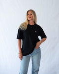 Das Model trägt ein schwarzes Bio-Baumwoll Shirt mit dezent gesticktem Wein Glas Motiv