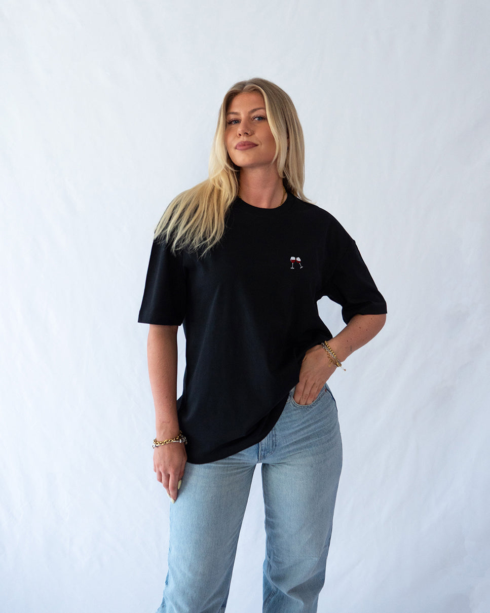 Das Model trägt ein schwarzes Bio-Baumwoll Shirt mit dezent gesticktem Wein Glas Motiv