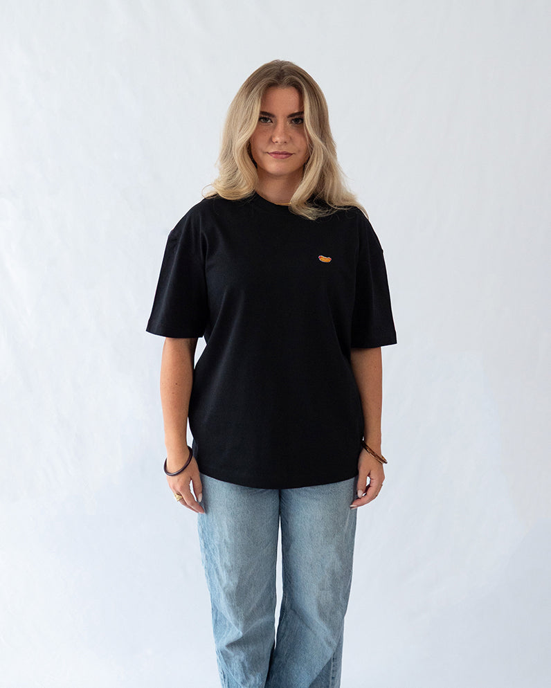 Das Model trägt ein schwarzes Bio-Baumwoll oversize Shirt mit gesticktem Hot Dog Motiv auf der Brust