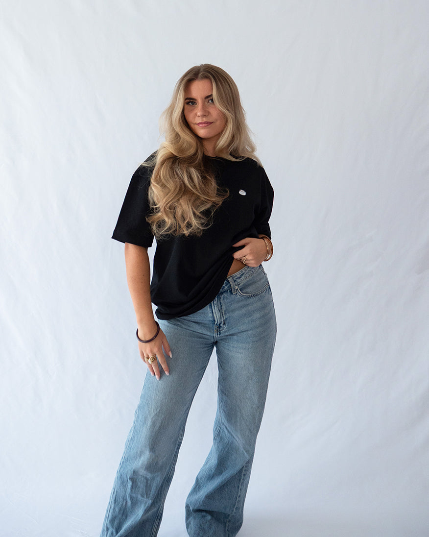 Das Model trägt ein schwarzes Bio-Baumwoll Shirt mit dezent gesticktem Kaffee mit Latte Art Motiv auf der Brust