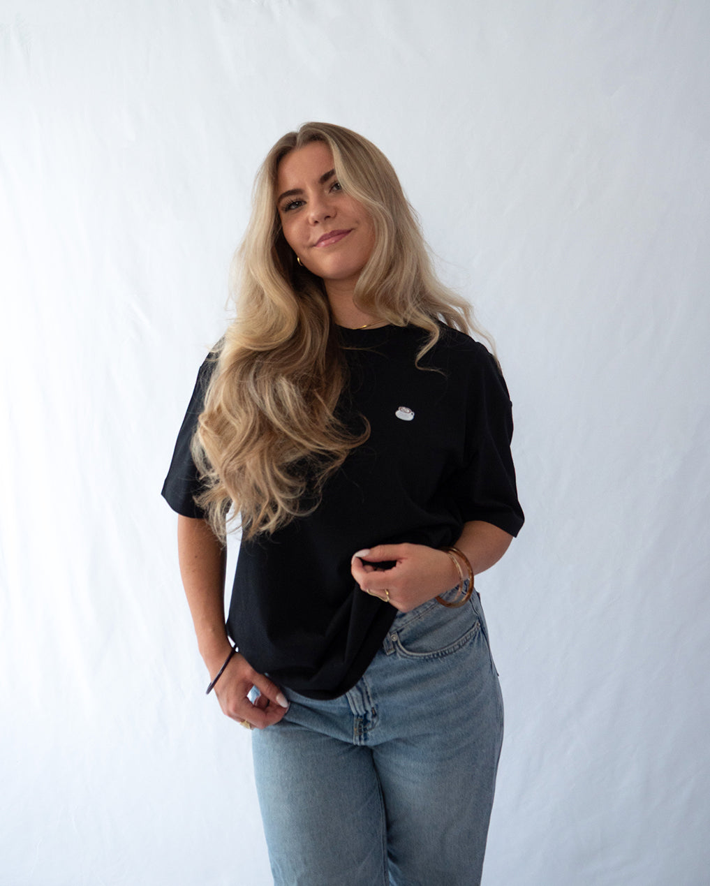 Das Model trägt ein schwarzes Bio-Baumwoll Shirt mit dezent gesticktem Kaffee mit Latte Art Motiv auf der Brust