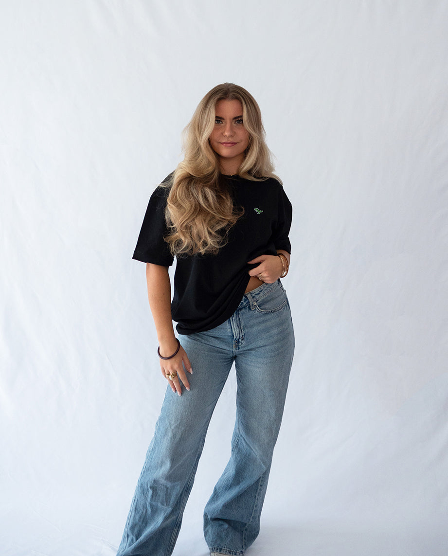 Das Model trägt ein schwarzes oversize Bio-Baumwoll T-Shirt mit gesticktem T-Rex Motiv auf der Brust