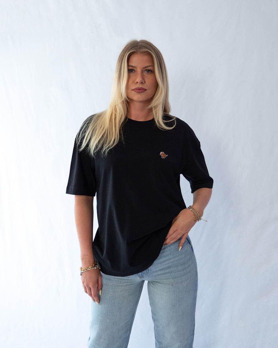 Das Model trägt ein schwarzes oversize Bio-Baumwoll T-Shirt mit gesticktem Triceratops Motiv auf der Brust