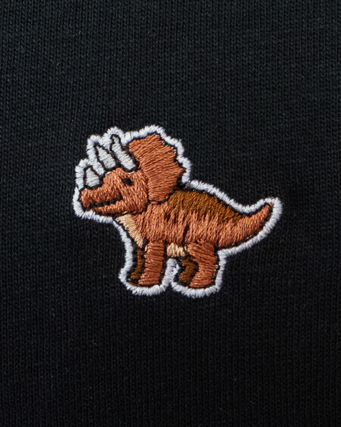 Nahaufnahme des gestickten Triceratops Motiv auf schwarzem T-Shirt