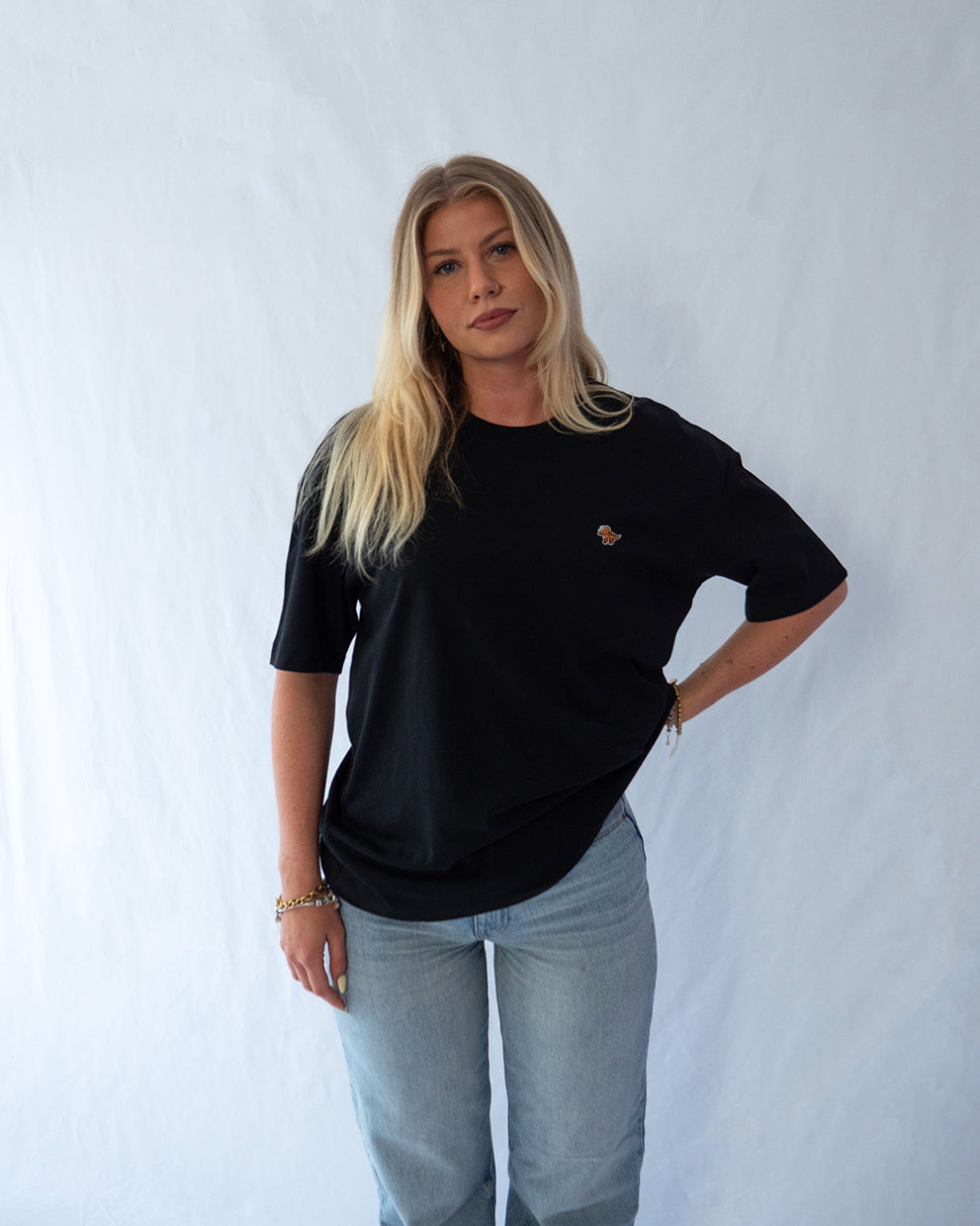 Das Model trägt ein schwarzes oversize Bio-Baumwoll T-Shirt mit gesticktem Triceratops Motiv auf der Brust