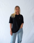 Das Model trägt ein schwarzes Bio-Baumwoll T-Shirt mit gesticktem Wildberry Cocktail Motiv auf der Brust