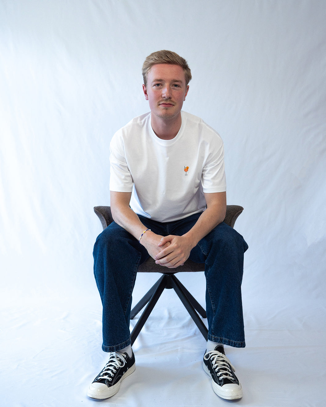 Das Model trägt ein weißes Bio-Baumwoll Shirt mit dezent gesticktem Aperol Spritz Motiv auf der Brust