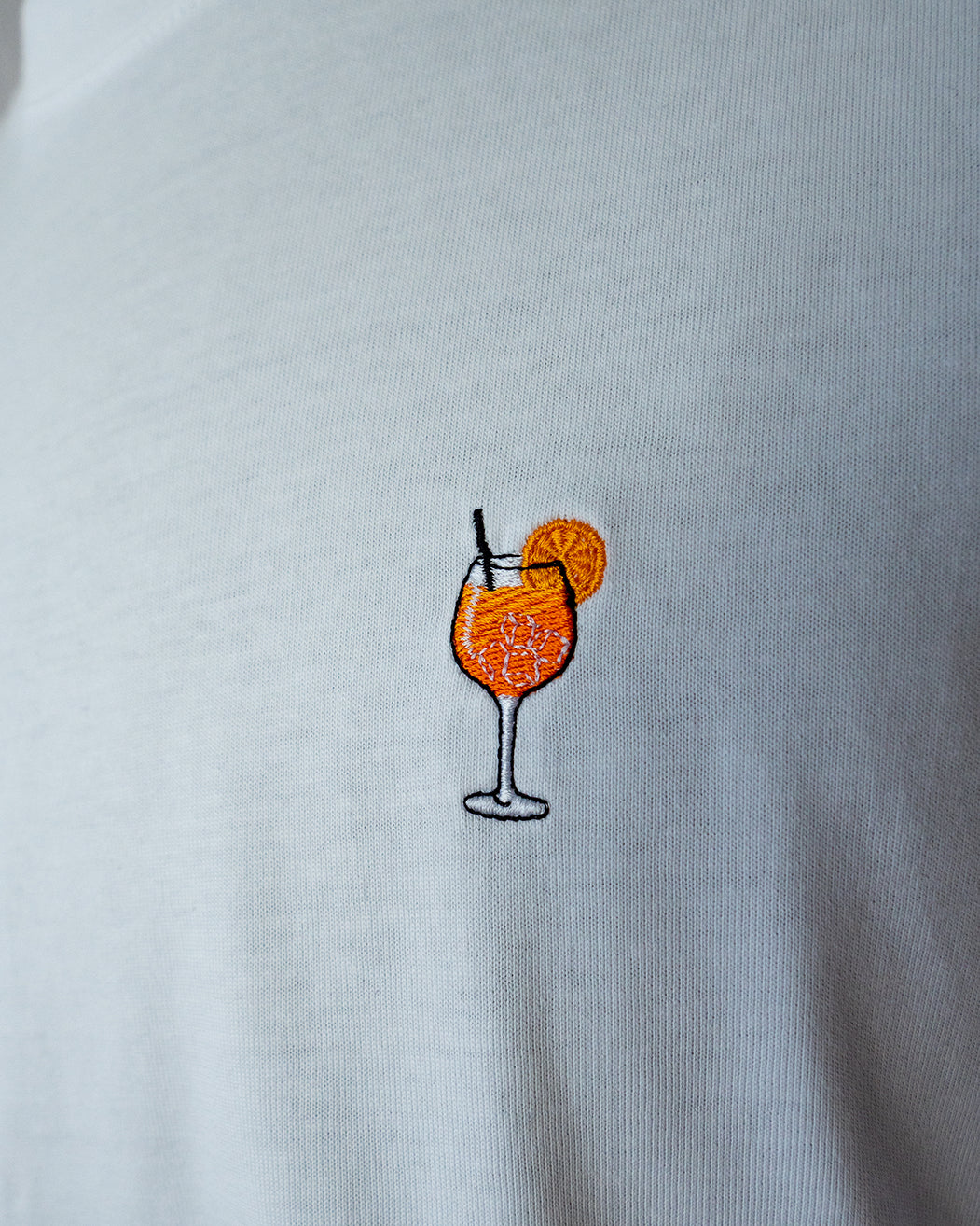 Nahaufnahme des gestickten Aperol Spritz Motiv auf weißem T-Shirt
