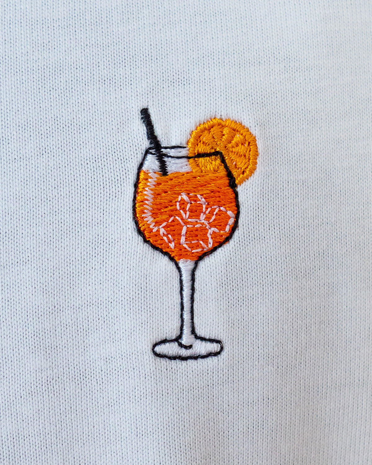 Nahaufnahme des gestickten Aperol Spritz Motiv auf weißem T-Shirt