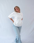 Das Model trägt ein weißes oversize Bio-Baumwoll T-Shirt mit gesticktem Brontosaurus Motiv auf der Brust