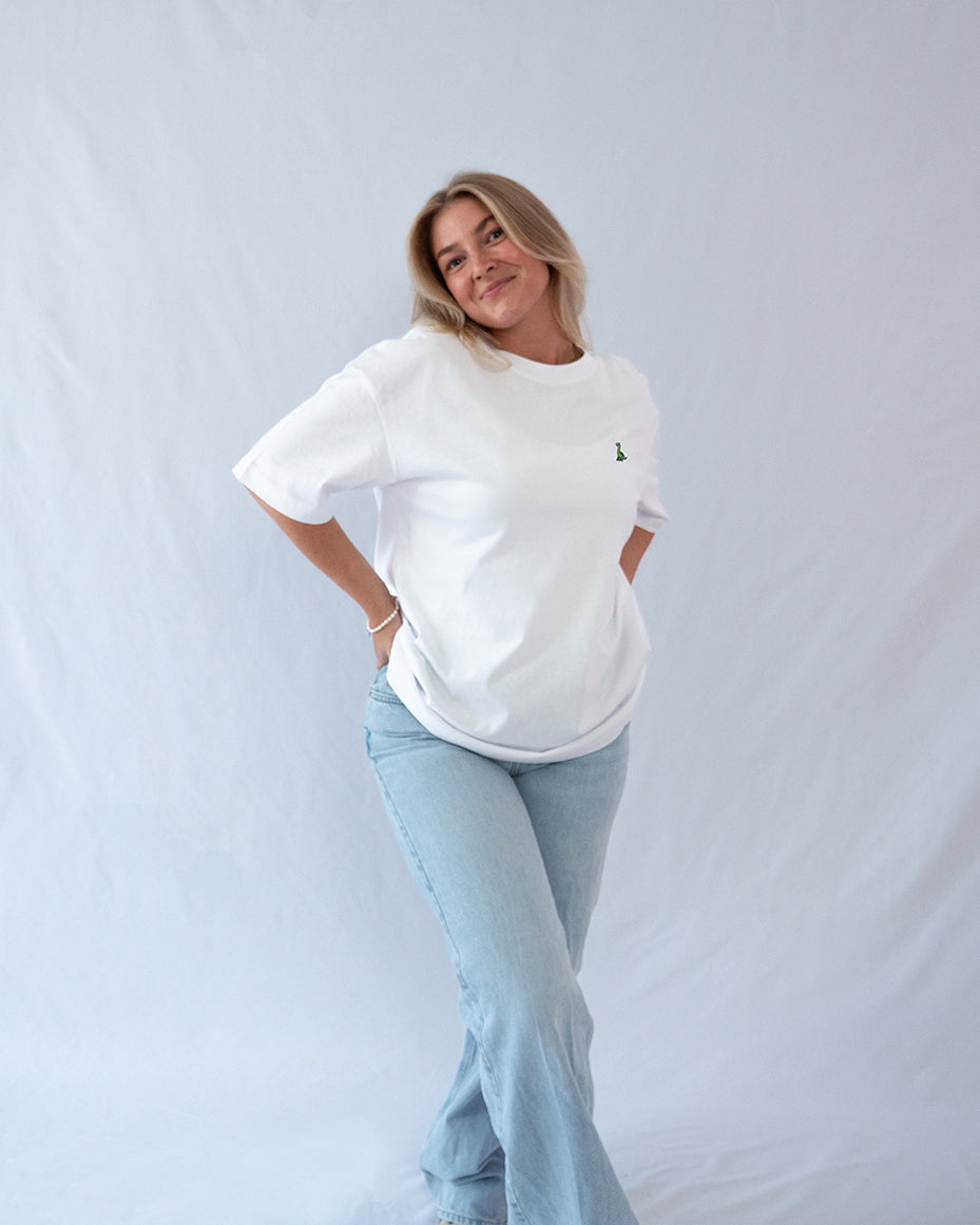Das Model trägt ein weißes oversize Bio-Baumwoll T-Shirt mit gesticktem Brontosaurus Motiv auf der Brust