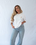 Das Model trägt ein weißes oversize Bio-Baumwoll T-Shirt mit gesticktem Croissant Motiv auf der Brust