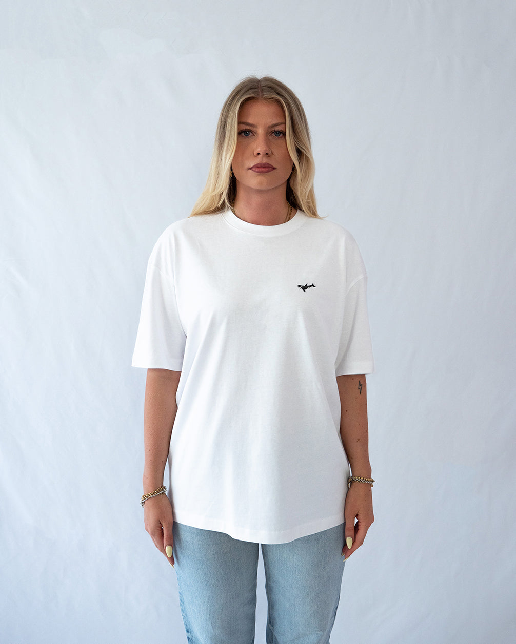 Das Model trägt ein weißes oversize Bio-Baumwoll T-Shirt mit gesticktem Orca Motiv auf der Brust
