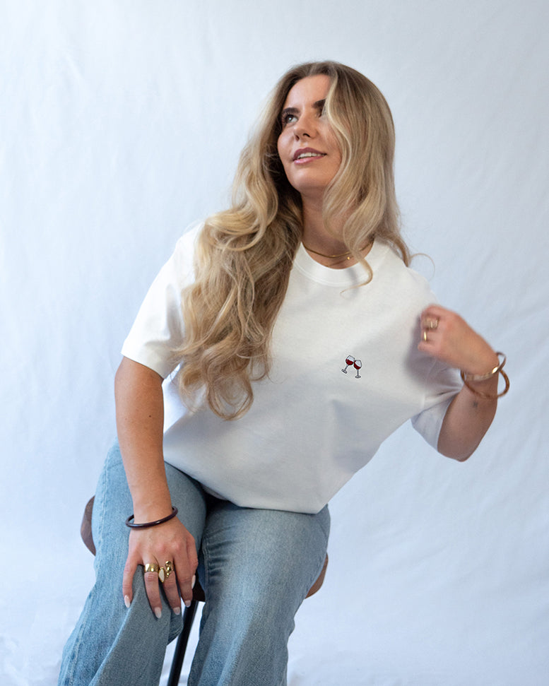 Das Model trägt ein weißes Bio-Baumwoll T-Shirt mit gesticktem Wein Glas Motiv