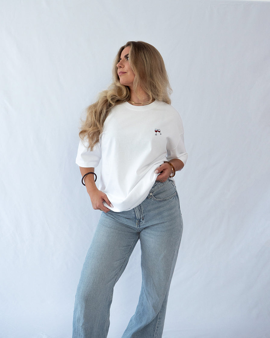 Das Model trägt ein weißes Bio-Baumwoll Shirt mit dezent gesticktem Wein Glas Motiv