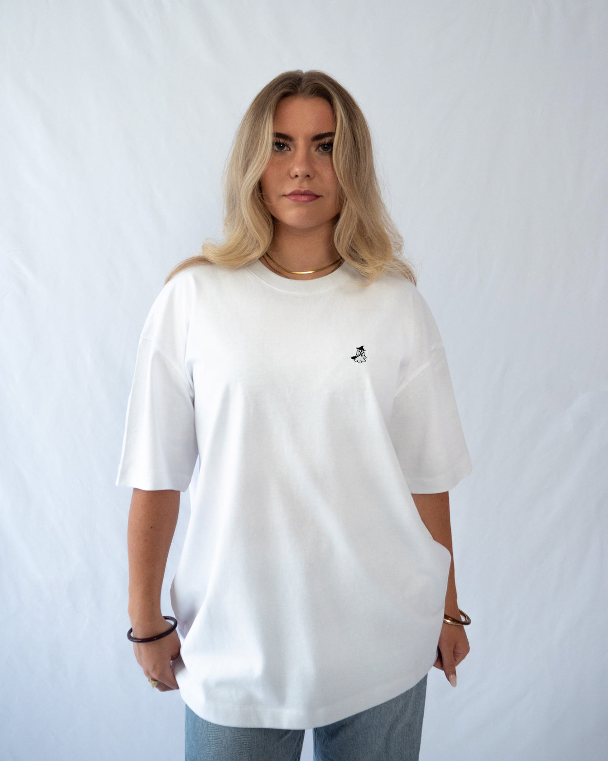 Das Model trägt ein weißes Bio-Baumwoll Shirt mit gesticktem Hexe Geist Motiv