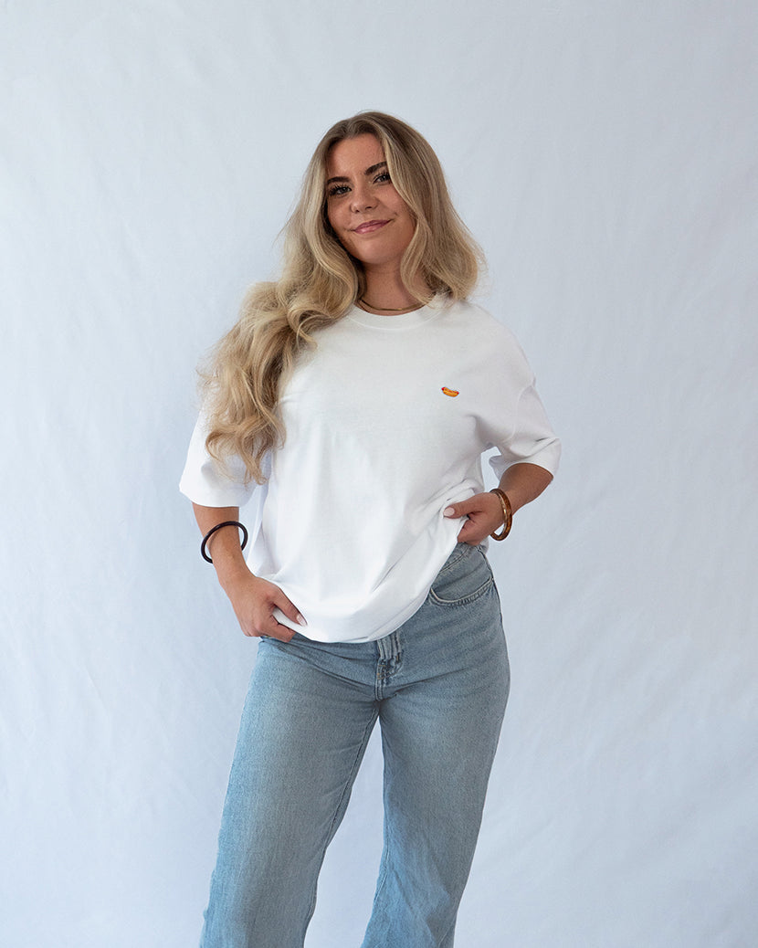 Das Model trägt ein weißes Bio-Baumwoll oversize Shirt mit gesticktem Hot Dog Motiv auf der Brust
