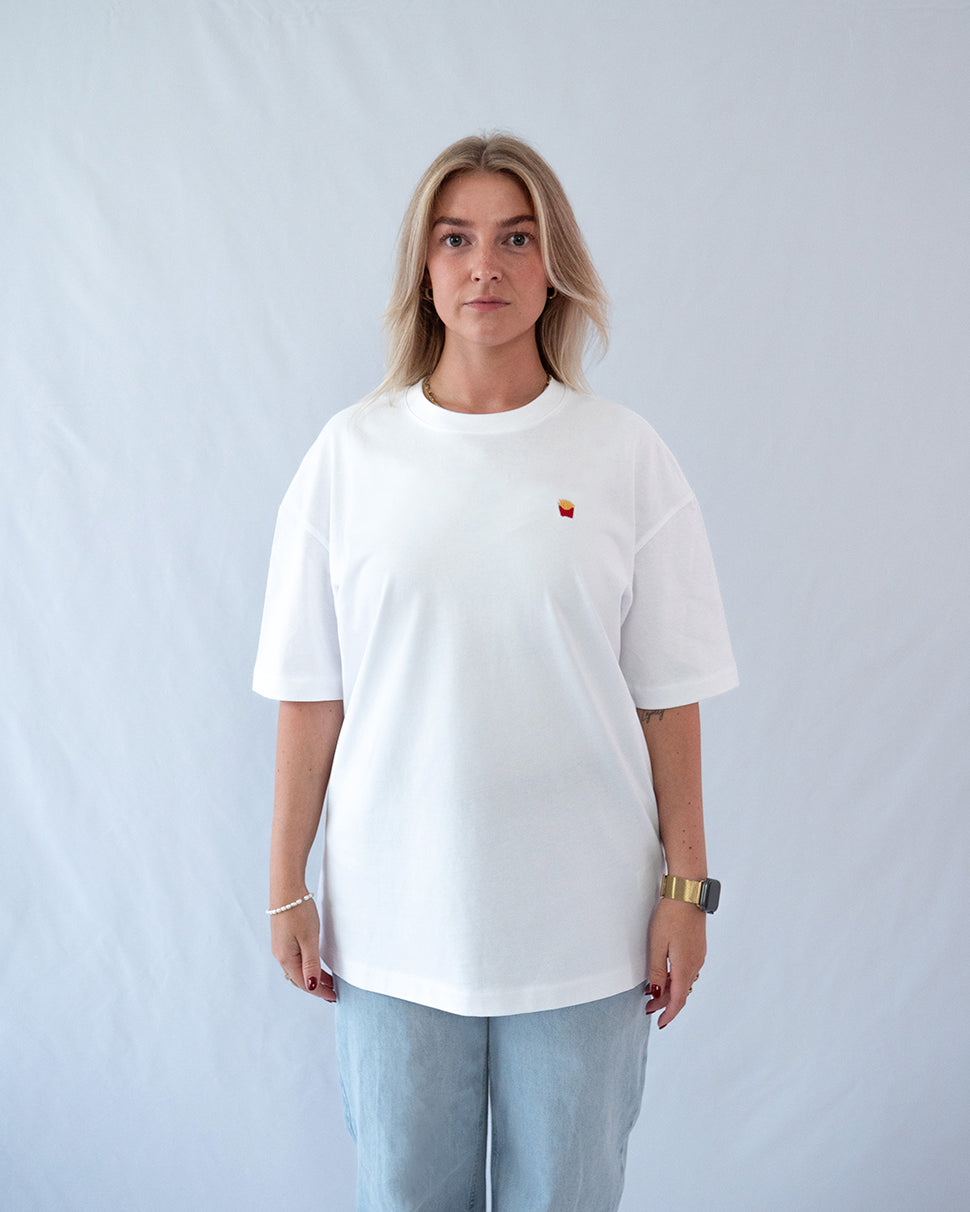 Das Model trägt ein weißes Bio-Baumwoll Shirt mit dezent gesticktem Pommes Motiv