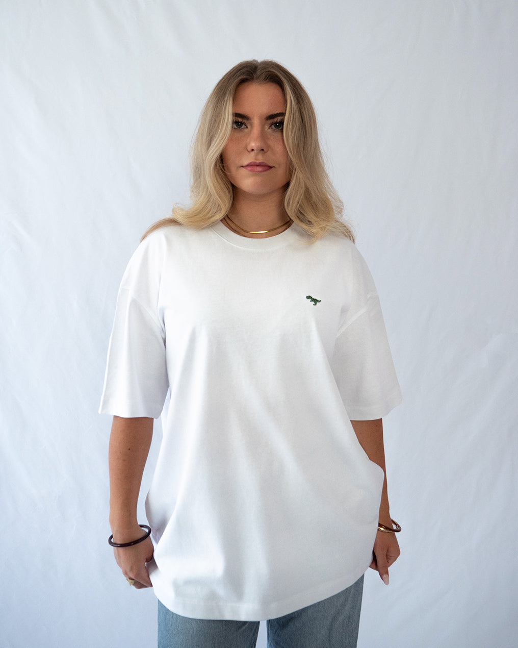 Das Model trägt ein weißes oversize Bio-Baumwoll T-Shirt mit gesticktem T-Rex Motiv auf der Brust