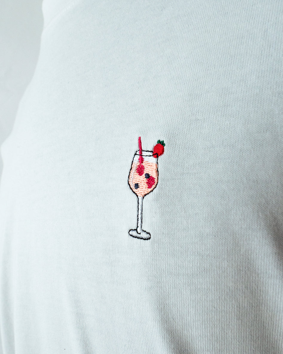 Nahaufnahme des gestickten Wildberry Cocktail Glas Motiv auf weißem T-Shirt