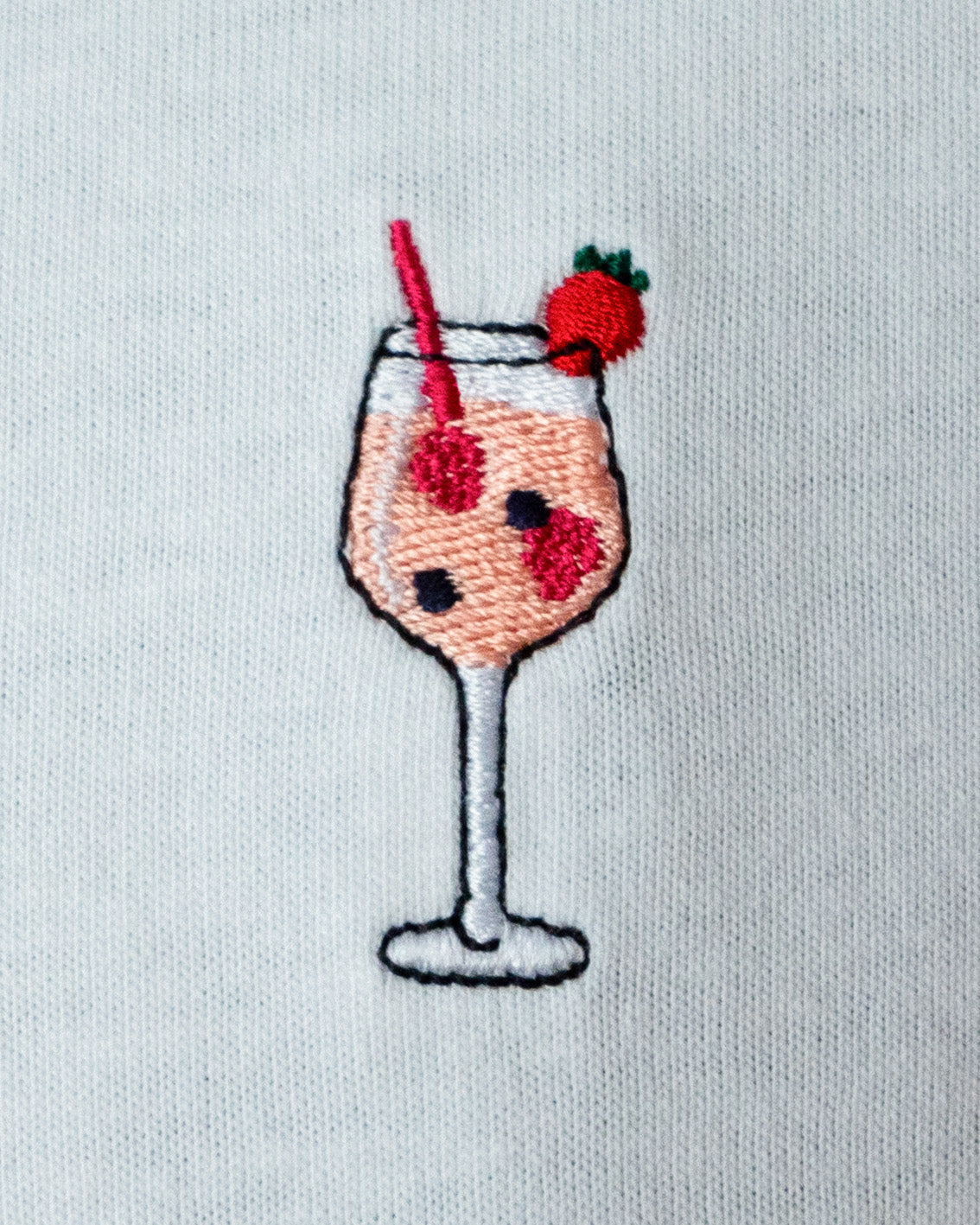 Nahaufnahme des gestickten Wildberry Cocktail Glas Motiv auf weißem T-Shirt